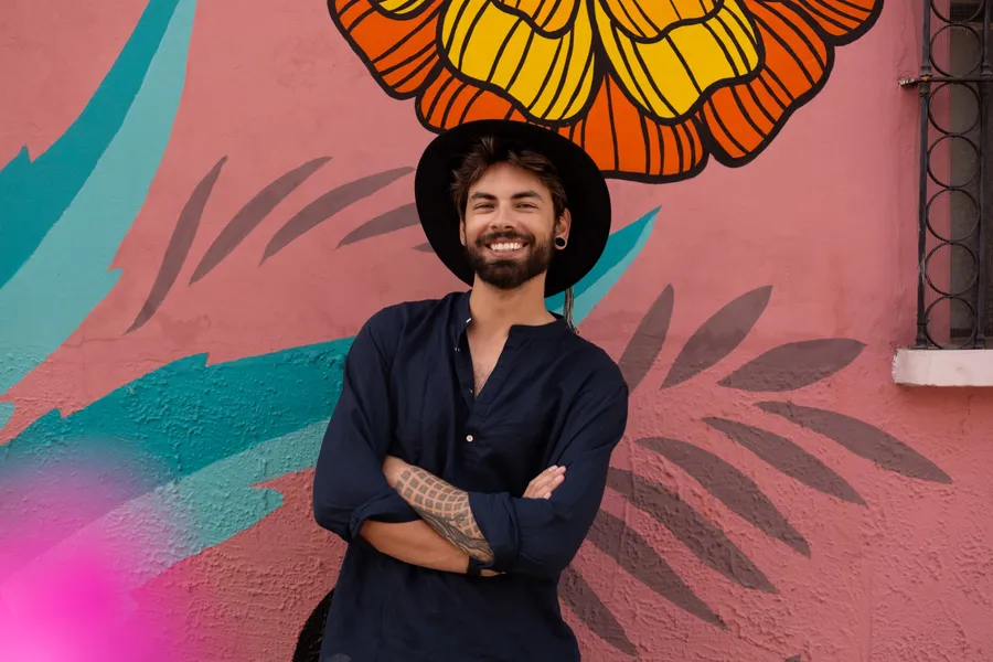 Arek Panek smiling in front of a pink mural with a large orange-and-yellow flower painted above him, taken in Oaxaca.